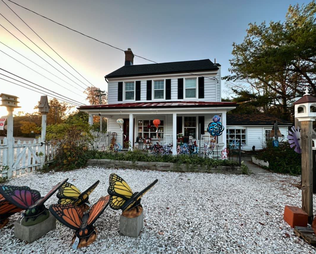 Front view of Feathered Nest with white house with the beautiful decor outside, porch displays and butterfly decor
